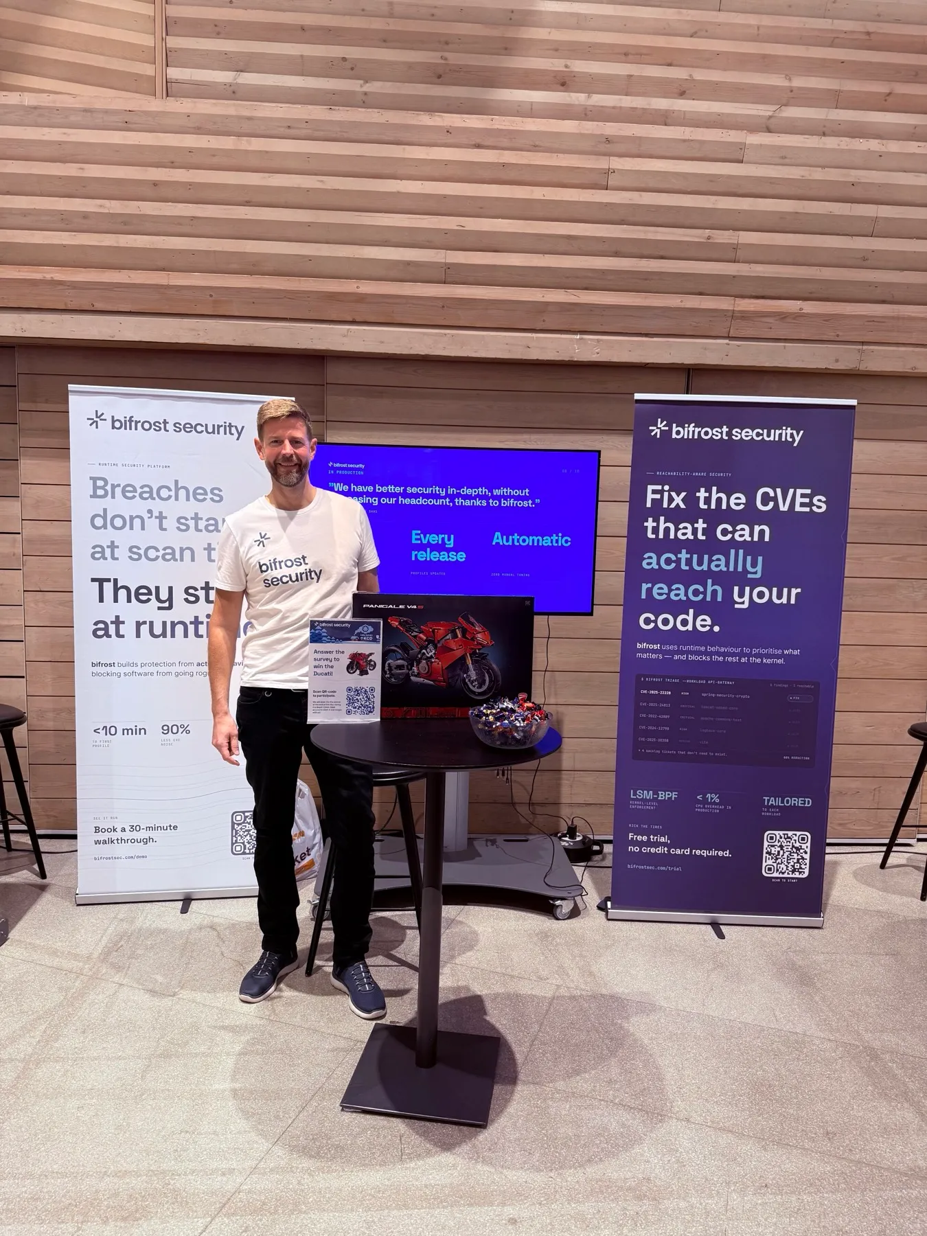 The bifrost security booth at KCD Helsinki, with roll-ups, a demo screen, and the LEGO survey prize on the table.